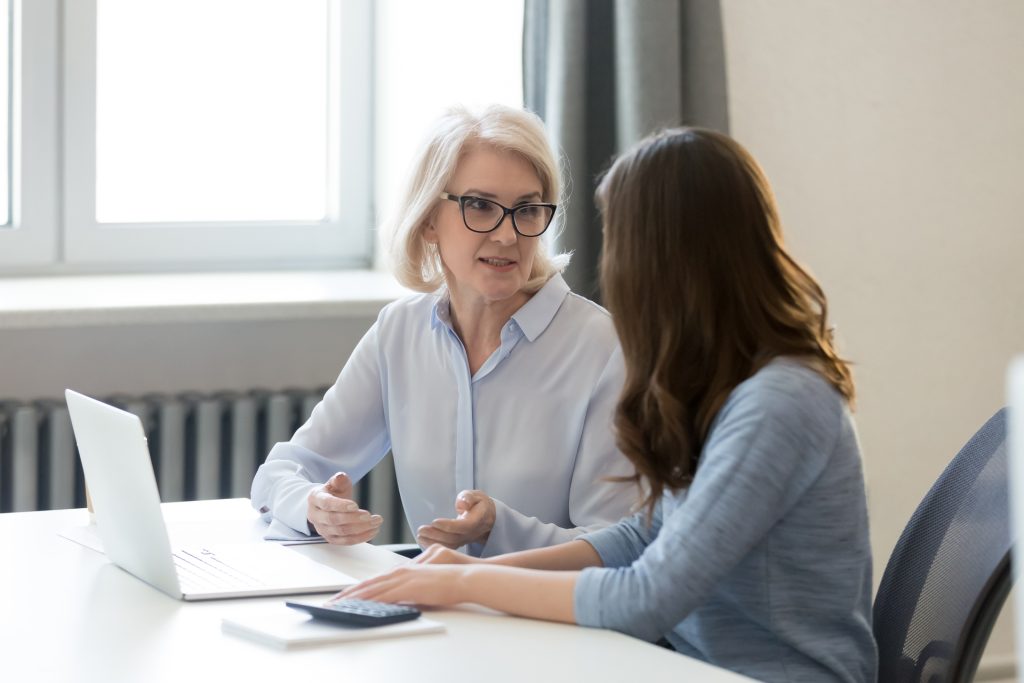 Vrouw die uitleg geeft aan een andere vrouw achter de laptop.