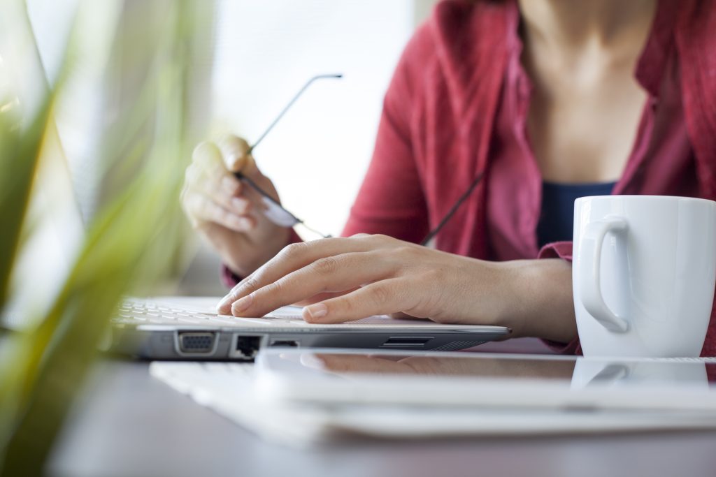 Vrouw met een bril in de hand is aan het typen.
